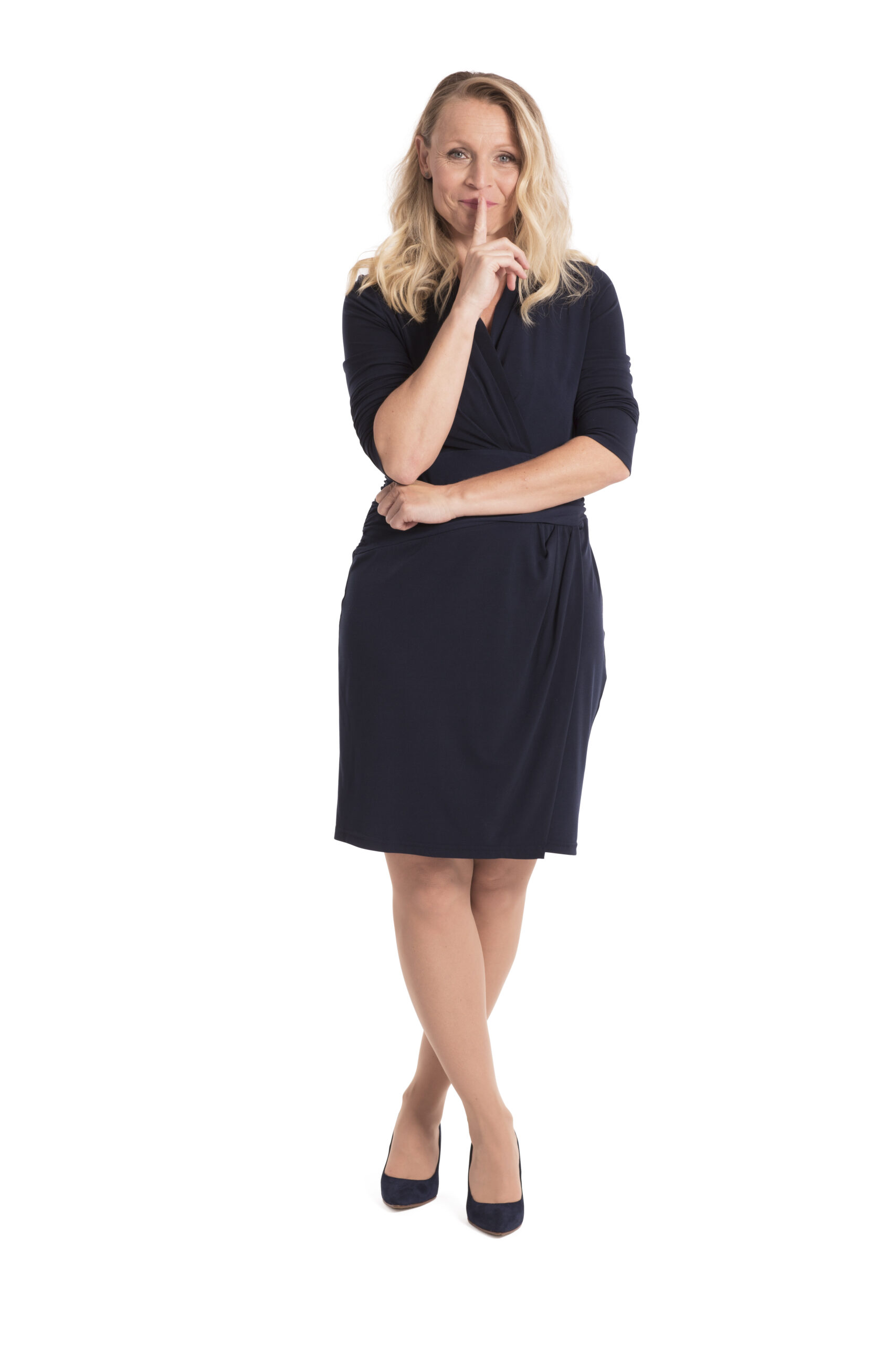 Woman standing crossing her legs and holding her finger up to her mouth.