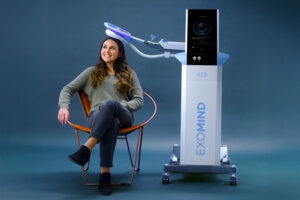 Woman sitting smiling with an Exomind device gently touching her head.