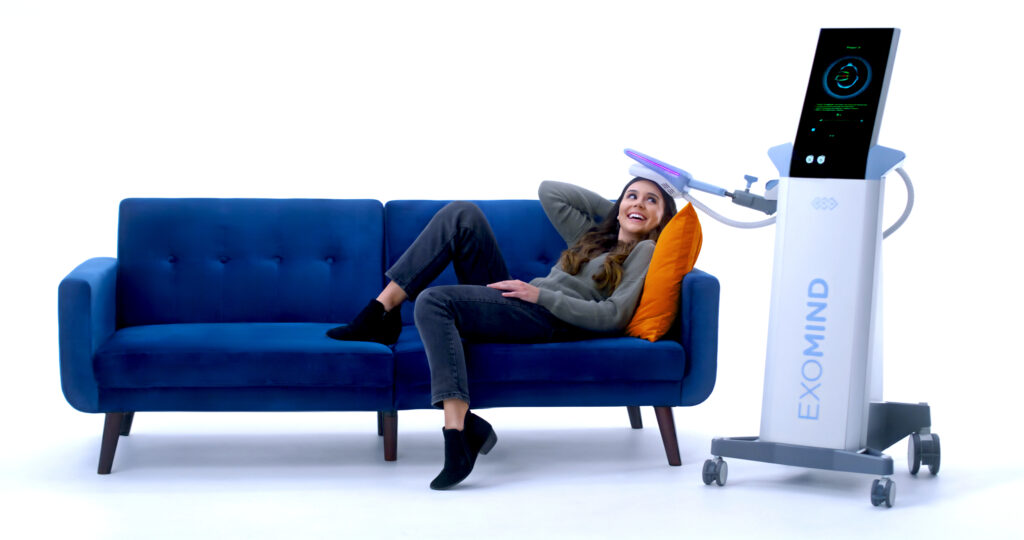 Exomind Female model on couch Woman laying on blue couch smiling comfortable with EXOMIND device on her head